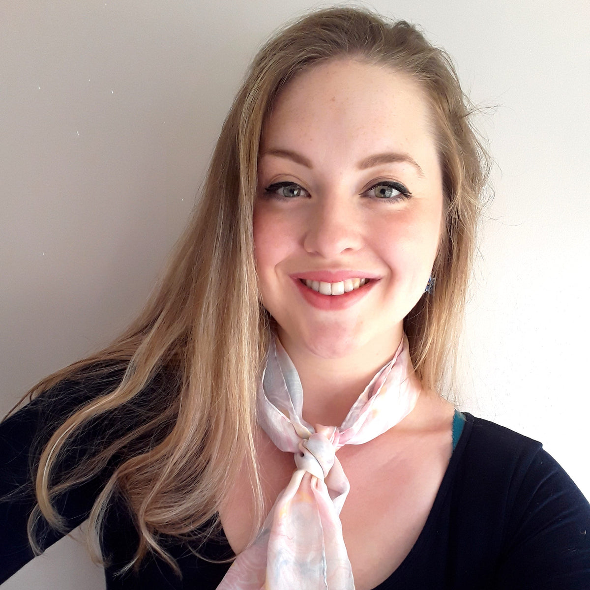 Woman wearing a light pink scarf with a subtle pattern against a plain background