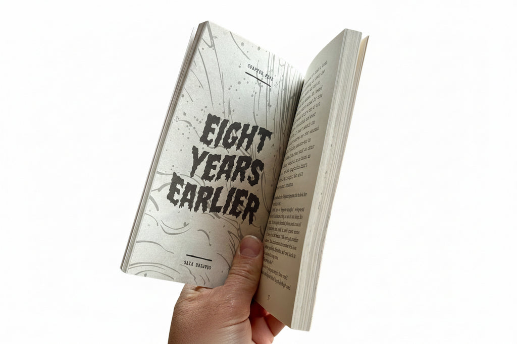 Book open to a page with 'Eight Years Earlier' text, held by a hand on a white background